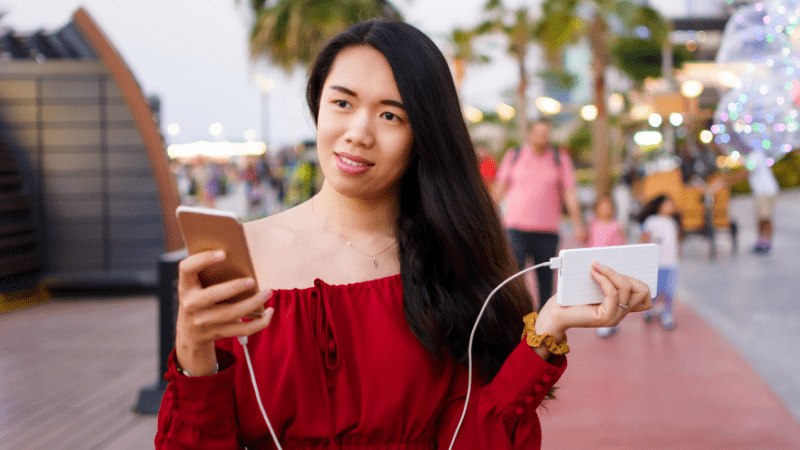 woman using a cell phone connected to a power bank, one of the things people forget to pack