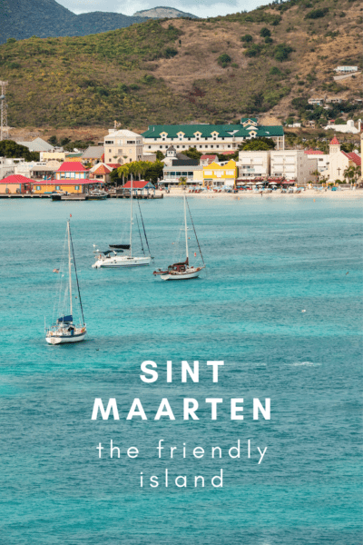 boats at anchor with small town and hill in background.. Text overlay says sint maarten the friendly island