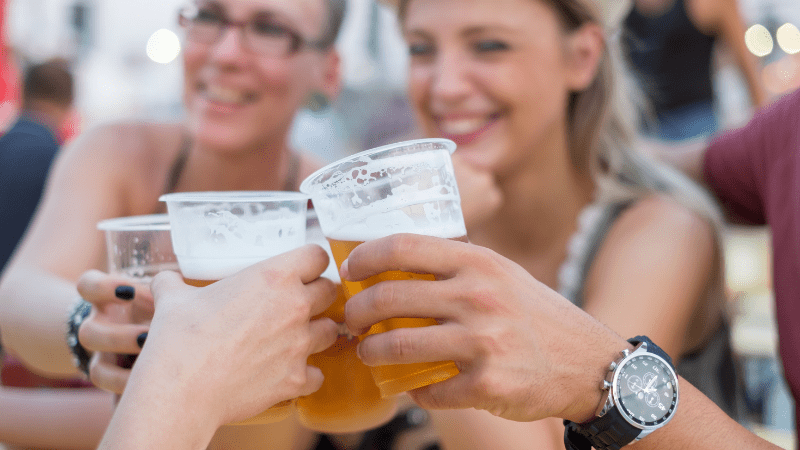 hands holding cups of beer. Smiling woman in background.