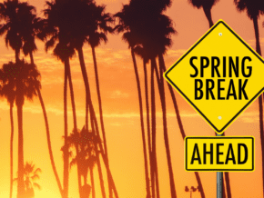 palm trees silhouetted against an orange sunset sky. Sign says spring break ahead. 