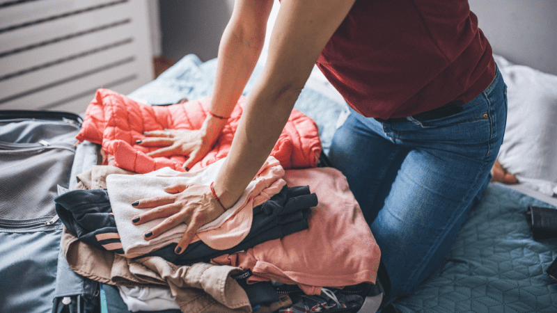 closeup of someone trying to stuff too many clothes into a suitcase. Obviously they need these suitcase packing tips and tricks, right?