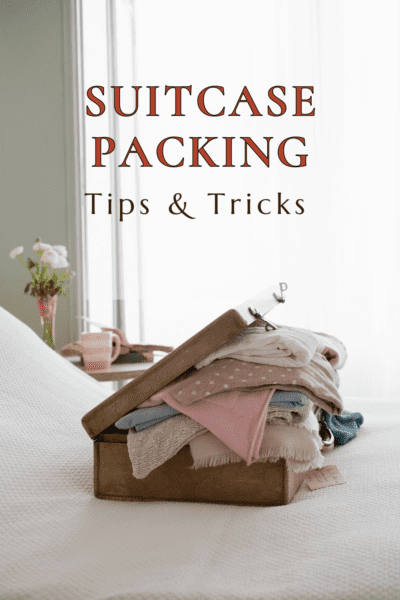 overstuffed suitcase on a bed with vase of flowers in background. Text overlay says "suitcase packing tips & tricks"