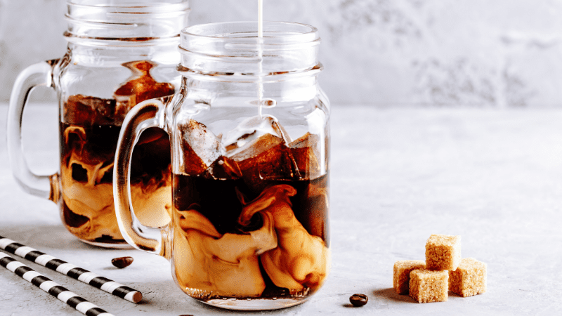 two mugs of thai coffee with milk at the bottom and cubes of demerara sugar on the table