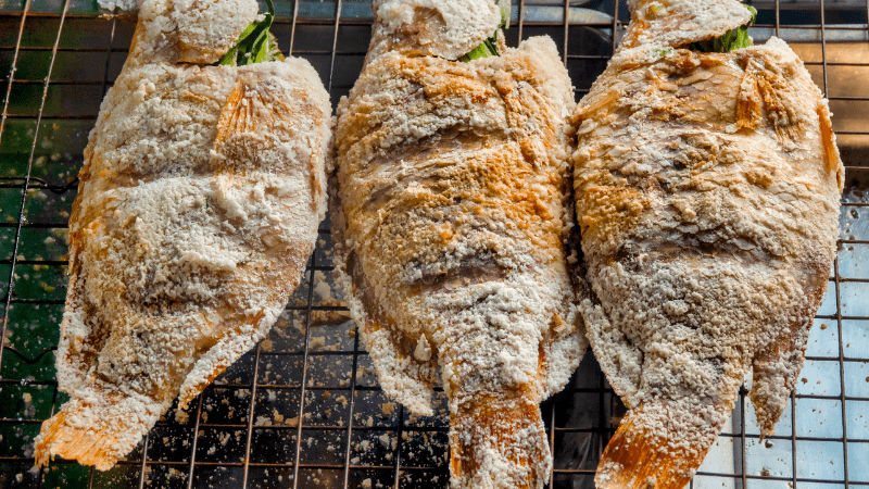 three grilled fish on a thai street food cart