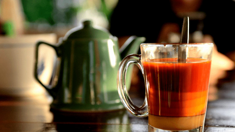 glass of thai tea with teapot in background