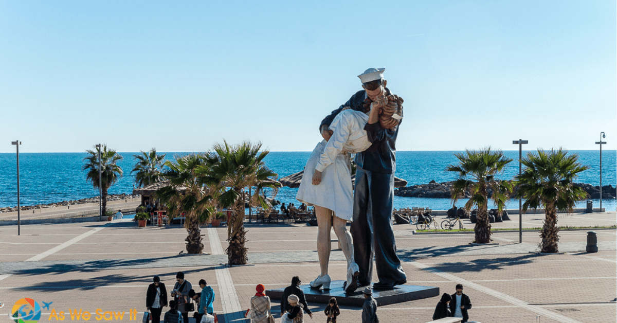 People standing around a statue of a sailor kissing a nurse on Civitavecchia's waterfront.