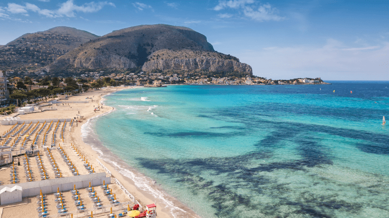 mondello beach chairs on the white sand with cliffs in background