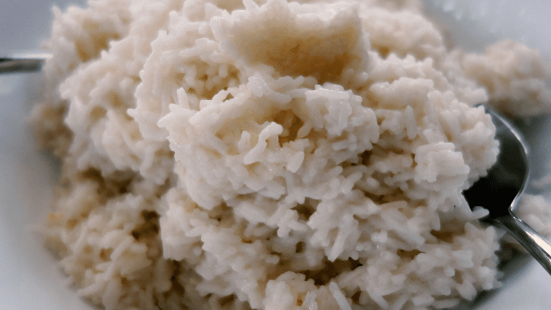 creamy coconut rice on a plate. foreground: spoon holding some coconut rice for a closer look