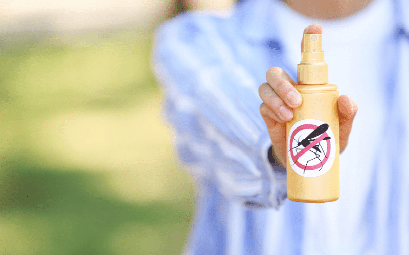 out-of-focus hand holding a spray bottle with a "no mosquito" sticker on it