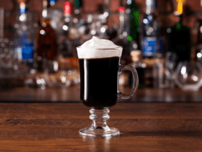 Mug of Irish coffee with shelves full of colorful bottles in background.