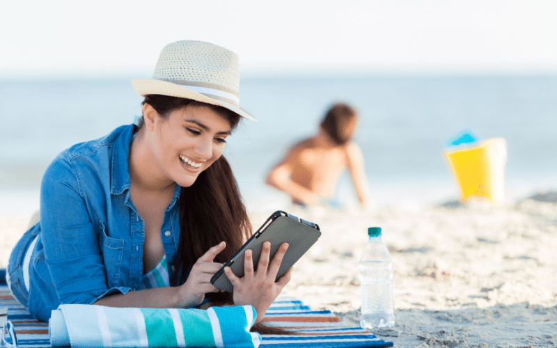 woman laying on a towel at the beach, reading an e reader