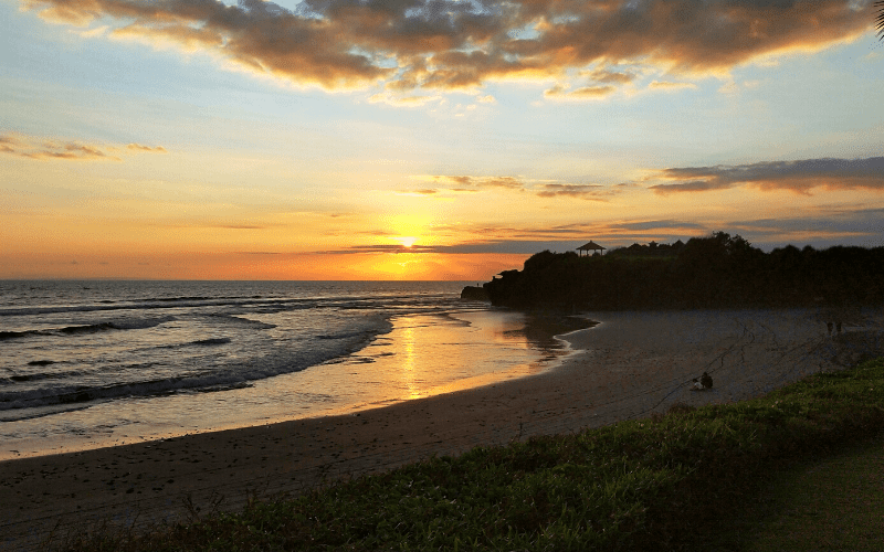 Sunset over a beach in Bali. Person sitting on beach.