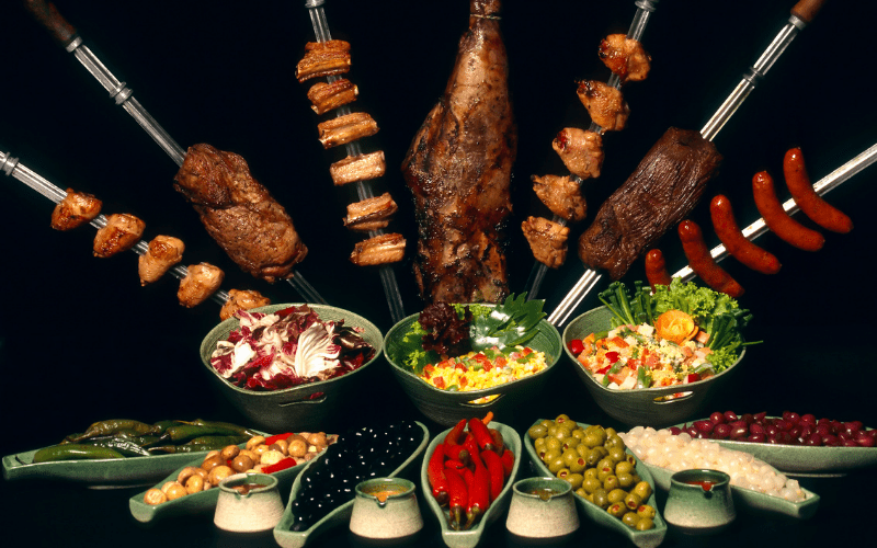 dishes of Brazilian food and skewers of beef churrasco