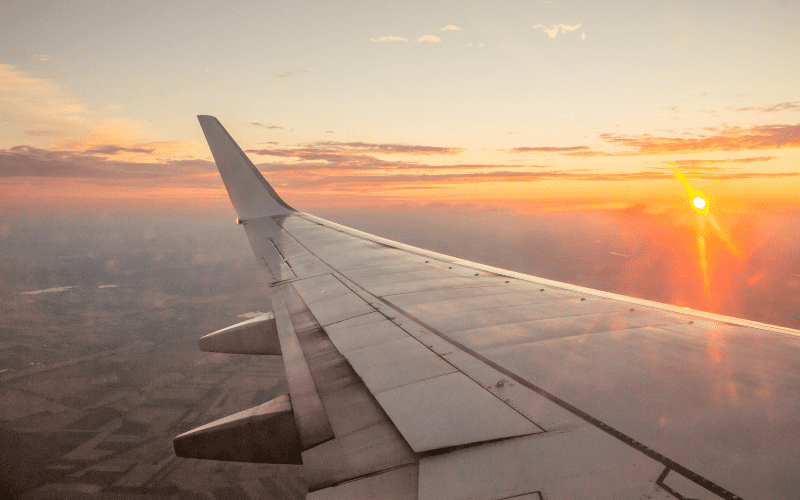 wing of a plane in flight with sunset in background