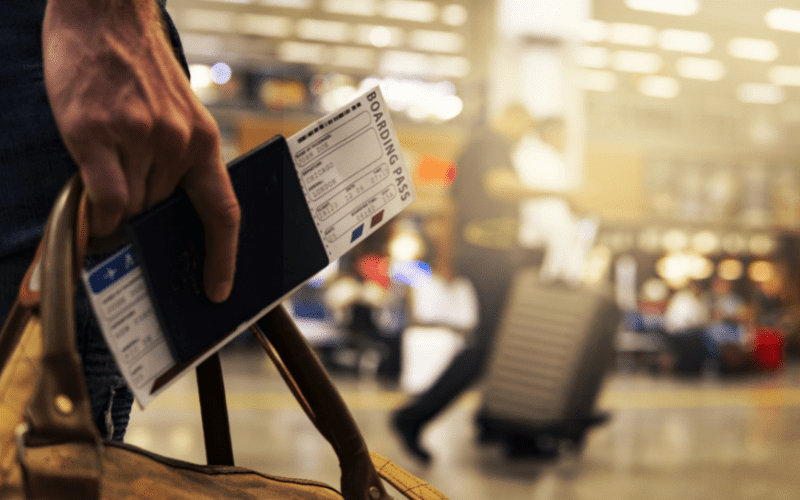 hand holding a plane ticket boarding pass with airport in background