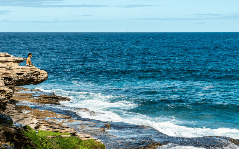 man sitting on a rock and overlooking the ocean