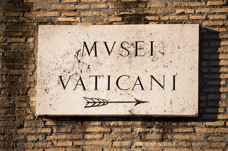 Vatican Museum guide. Sign with an arrow pointing to the right below the Latin words MVSEI VATICANI, showing location Vatican Museums.