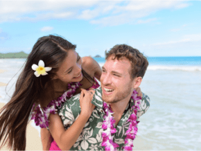 Young couple wearing leis on a beach.