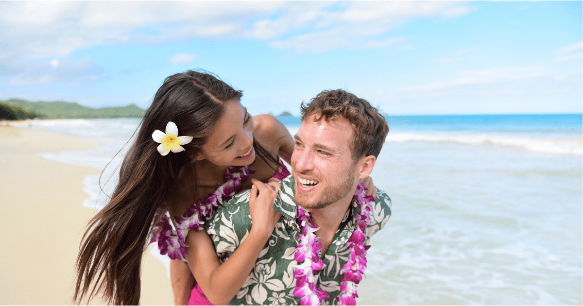 Young couple wearing leis on a beach.