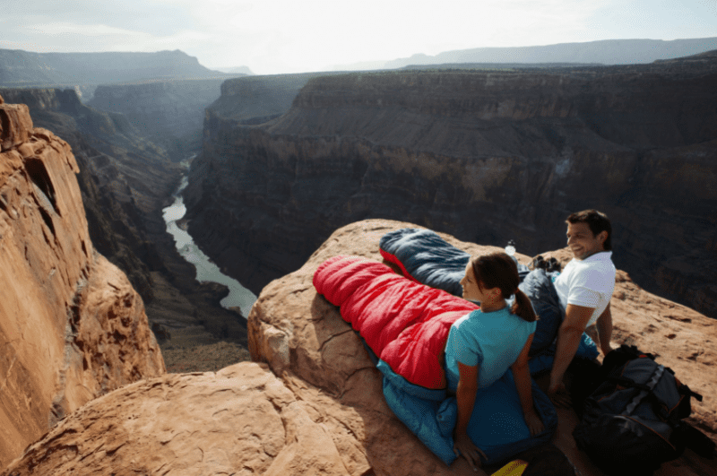 two people on a cliff looking at the river below them in the background