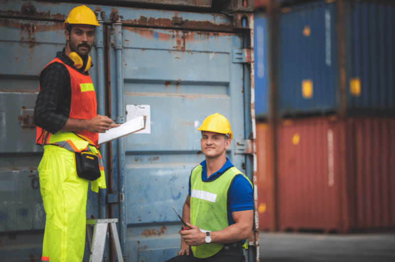 two workers in front of a container shipping a car to South America 