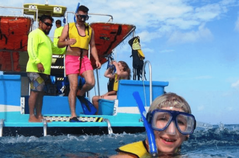 Child in foreground with mask and snorkel. Glass bottom boat in the background with people on it