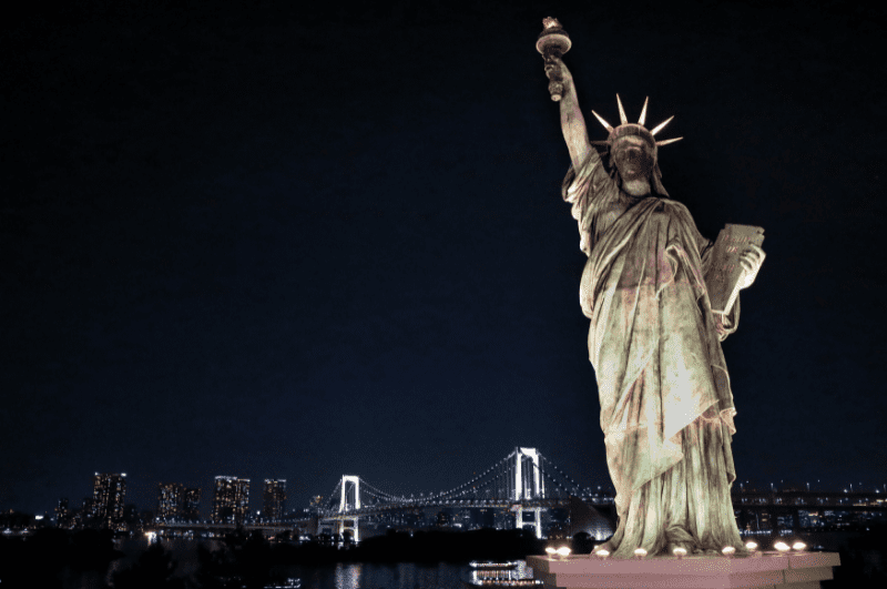 NY City at night: Here, the Statue of Liberty stands in New York Harbor, with the Verrazano [Narrows] Bridge illuminated in the background