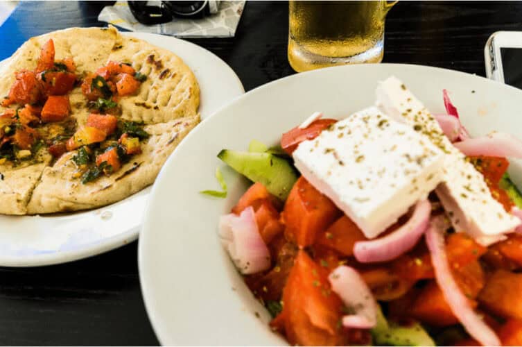Greek salad topped with a hunk of feta cheese. Plate of pita bread on the side