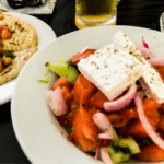 Greek salad topped with a hunk of feta cheese. Plate of pita bread on the side