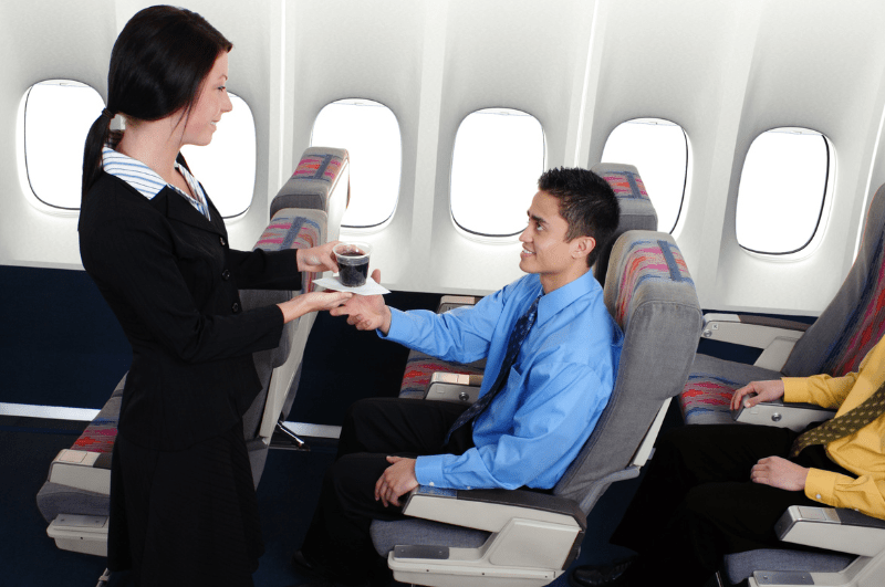 flight attendant serving a man a drink on a plane