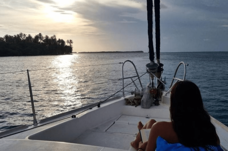 woman reading a book with an island and sunset in the distance. This is how to visit San Blas Islands Panama!
