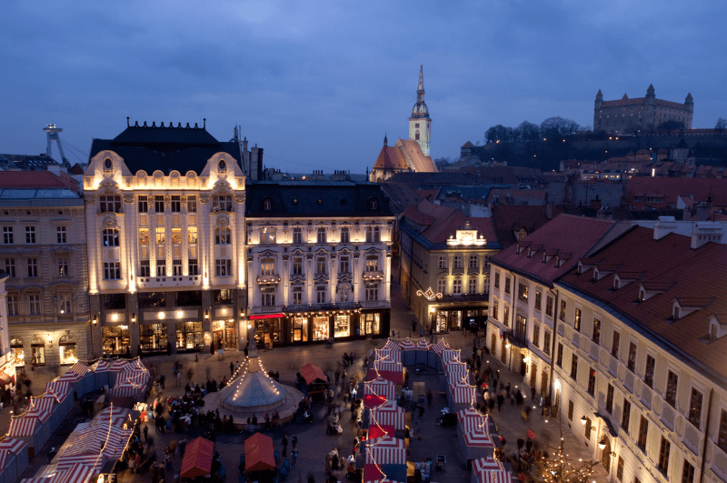 Christmas market in a square in bratislava with church and castle in background