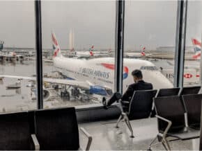 Man sitting in a chair in an airport with British Airways plane outside the window