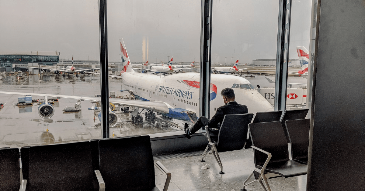 Man sitting in a chair in an airport with British Airways plane outside the window