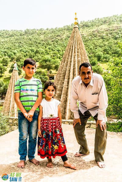 Yazidi father crouching next to his son and daughter, in front of a Yazidi rooftop