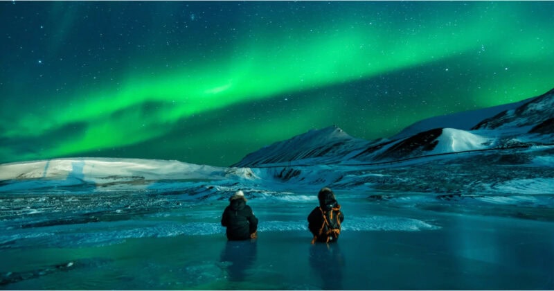 Two people in water, looking at the northern lights