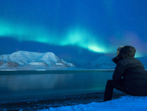 man sitting on snow, to see the northern lights
