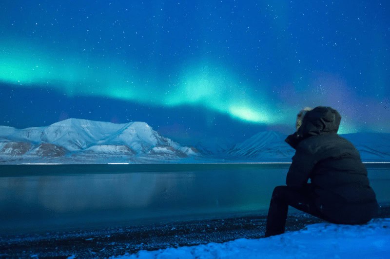 man sitting on snow, to see the northern lights