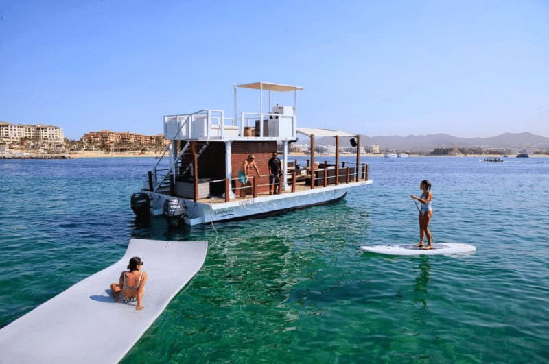 Catamaran anchored with two passengers enjoying the water on a float and a SUP board