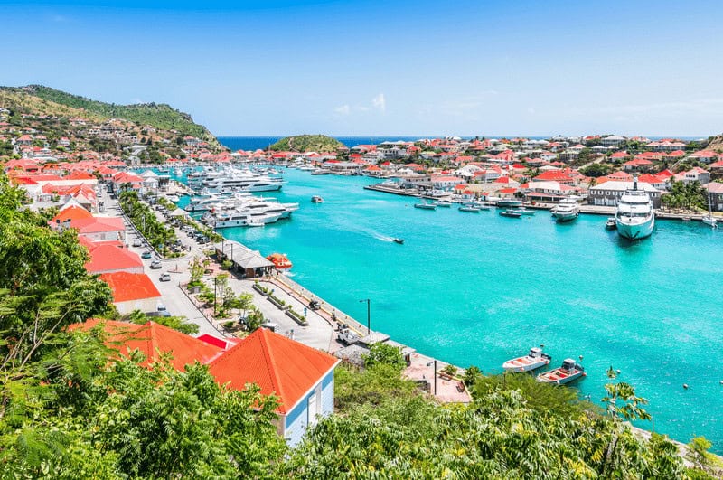 Boats bobbing in the brilliant blue water in the middle of a town. High end living in St. Barts.