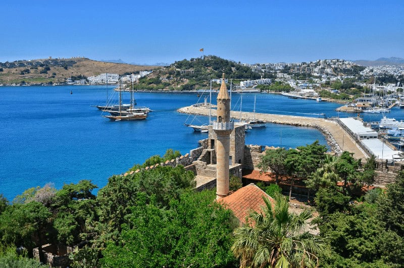Minaret in Bodrum Turkey with boats on a lake and a mountain in the background