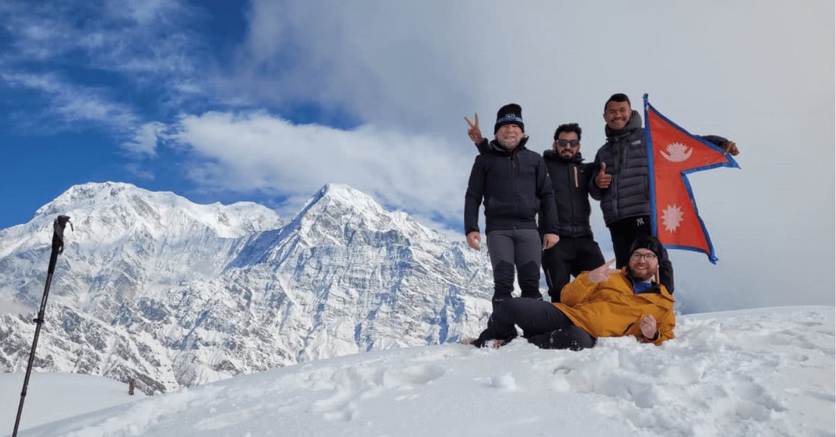 four people holding a flag on the Mardi HImal Trek