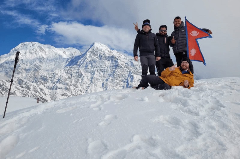 four people holding a flag on the Mardi HImal Trek