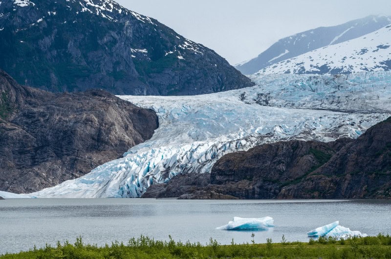 Mendenhall Glacier in Alaska. Water in foreground, tree covered hills on the side.