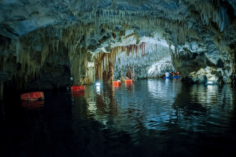 Stalactites and stalagmites in Diros Caves. Boat in the water in the distance.