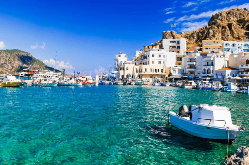 Pigadia Village on the island of Karpathos, one of the hidden gems in Greece. Boat and clear water in foreground.