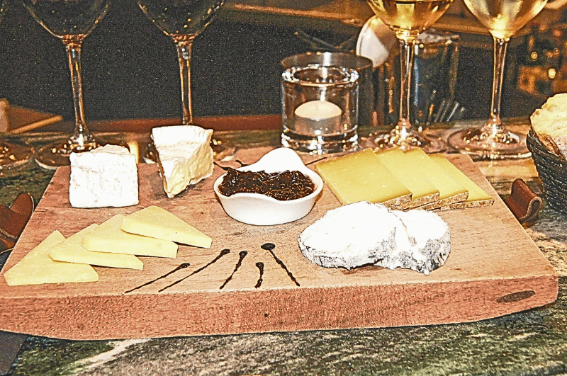 Cheese and jam on a wooden platter; glasses of white wine in background