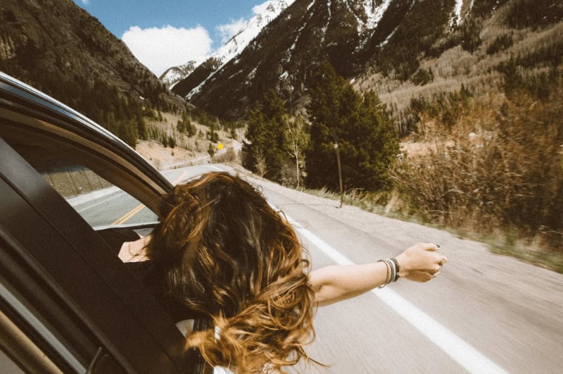 Woman passenger leaning her head and arm out the window on a road trip