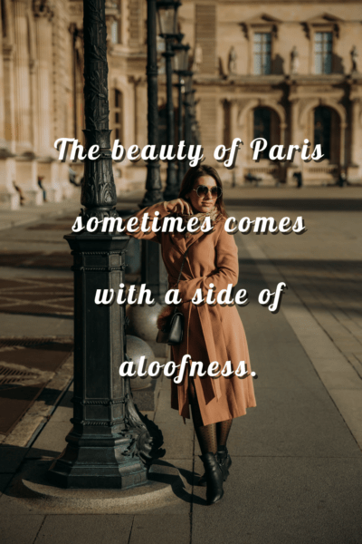 Woman leaning against a lamppost. The text overlay says "The beauty of Paris often comes with a side of aloofness."
