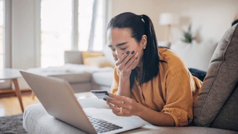 Upset woman looking at her credit card, her computer is on the desk
